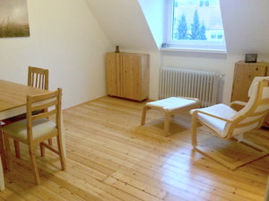 Minimalismus im Wohnzimmer: Links Tisch und 2 Stühle, rechts am Fenster: 2 Holzschränke und ein Sessel (Pöang von Ikea) mit Fußteil.