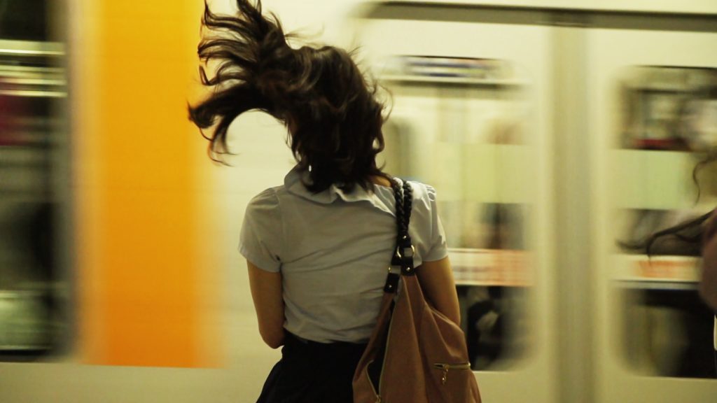 Frau von hinten fotografiert. Wehende Haare. Im Hintergrund verschwommen ein vorbeifahrender Zug.