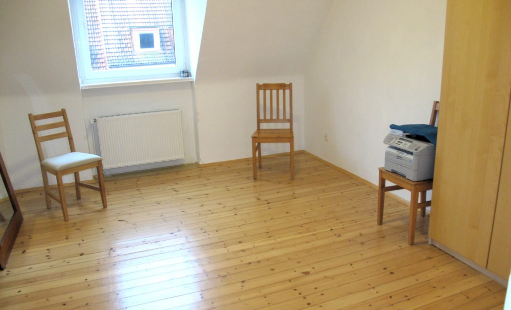 Wenige Möbel - ein Blick in ein fast leeres Zimmer: Stühle - auf einem Stuhl steht ein Drucker. Rechts im Bildrand ein Schrank. Am linken Bildrand ein unnutzer großer Spiegel.