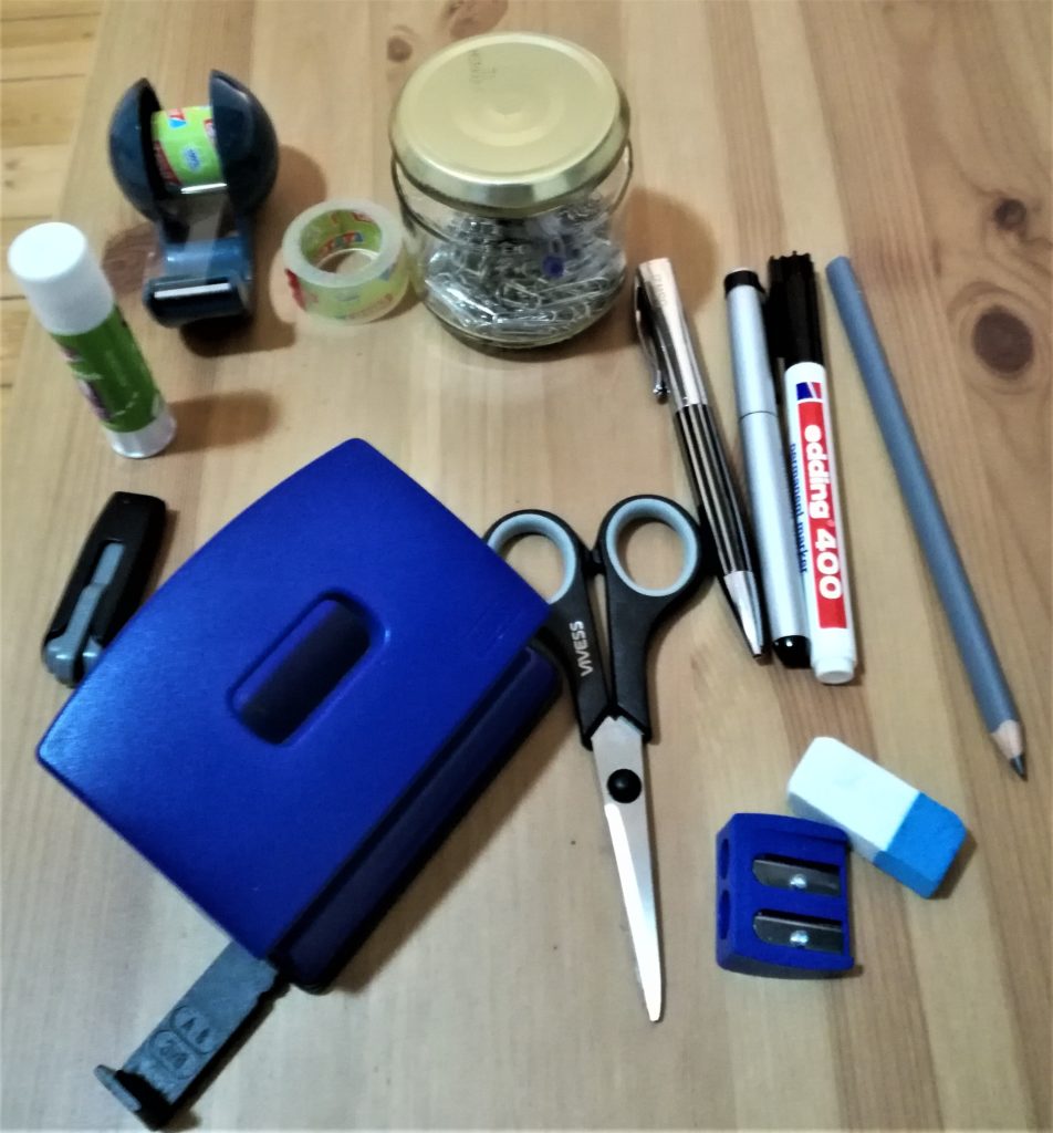 Kleinteile aus der schwarzen Kiste: Locher, USB-Stick, Klebestift, Klebefilmabroller, Glas mit Büroklammern, 1 Kugelschreiber, 1 Füller, 1 Bleistift, 1 Edding, 1 Radiergummmi, 1 Anspitzer