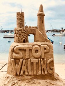 Eine Sandburg mit der Aufschrift: "Stop waiting"