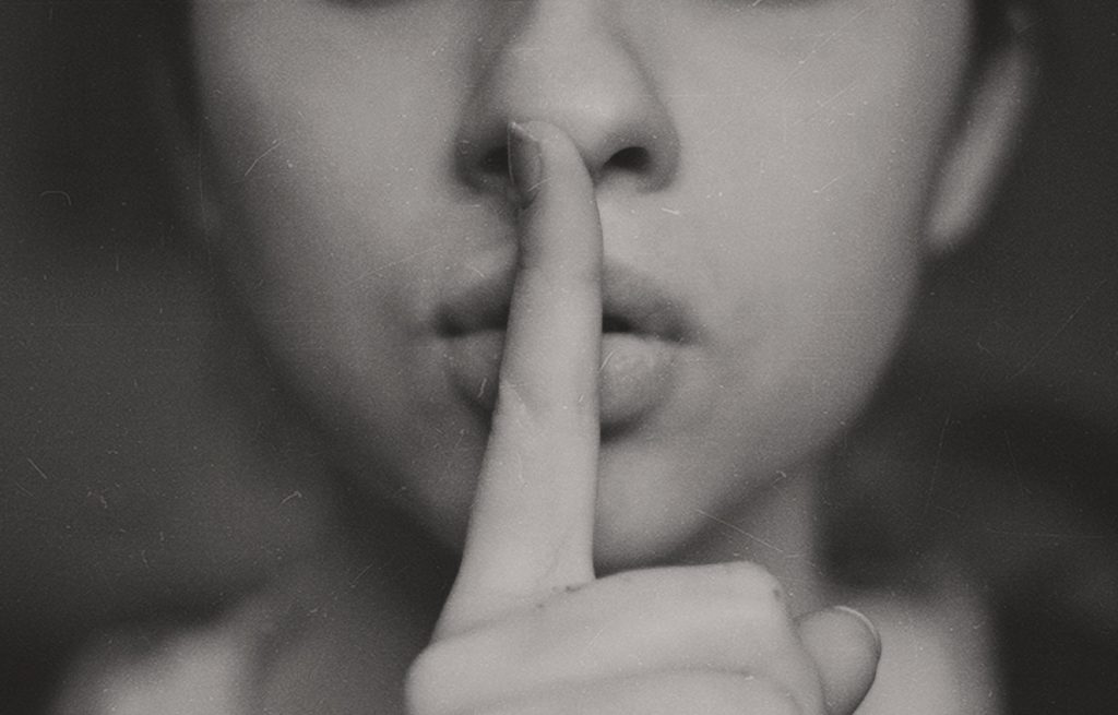 Eine Frau, die als Stille-Symbol den Zeigefinger vor den Mund hält