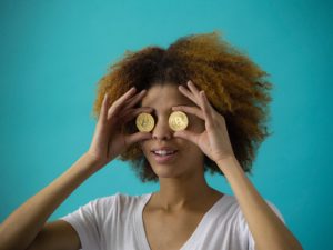 eine Frau hält zwei goldfarbene Bitcoin-Münzen vor ihre Augen