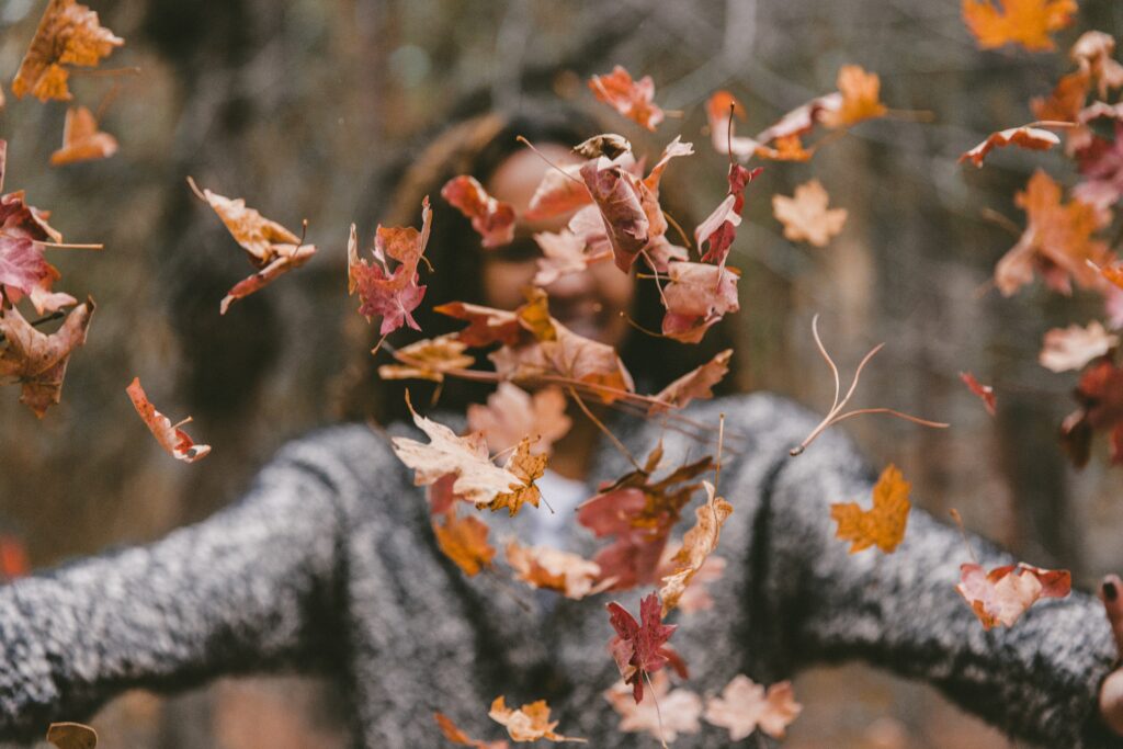 Eine lachende Frau wirft Herbstblätter durch die Luft