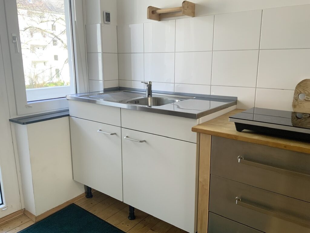 Weißer Unterschrank mit Auflagespüle, am rechten Bildrand ein Schubladenschrank (Värde, Ikea) mit Kochplatten darauf