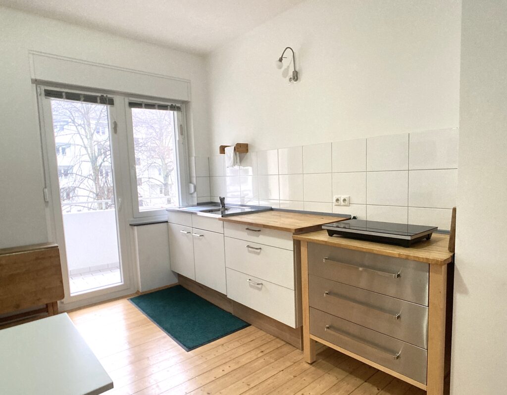 Blick auf Küchenzeile von links nach rechts: Spüle und 2 Schubladenschränke. Rechts eine Kochplatte.